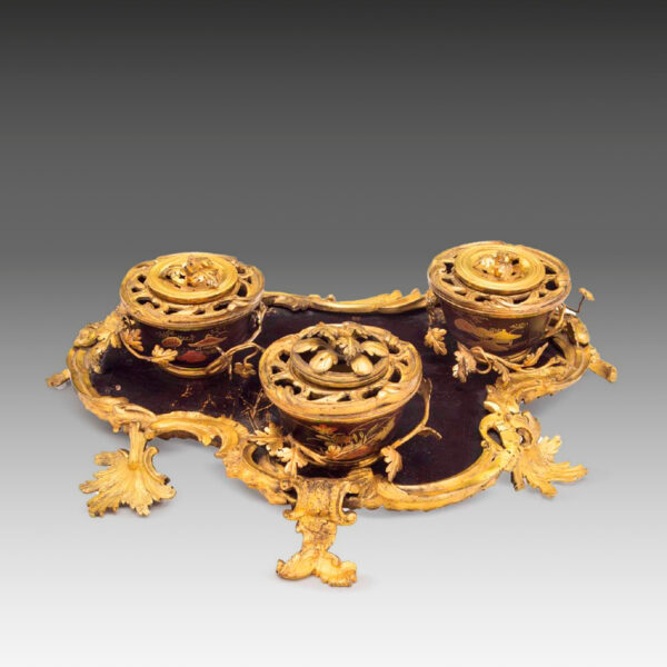 Le plateau en forme de cartouche serti de trois pots à couvercles percés ceinturés de vignes de fleurs, posés sur des supports feuillagés.